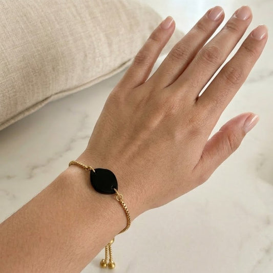 Hand wearing a gold bracelet with a black bead on a neutral background