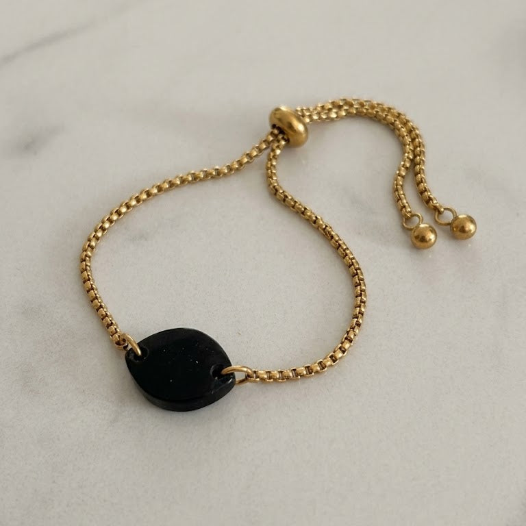 Gold bracelet with a black bead on a solid surface
