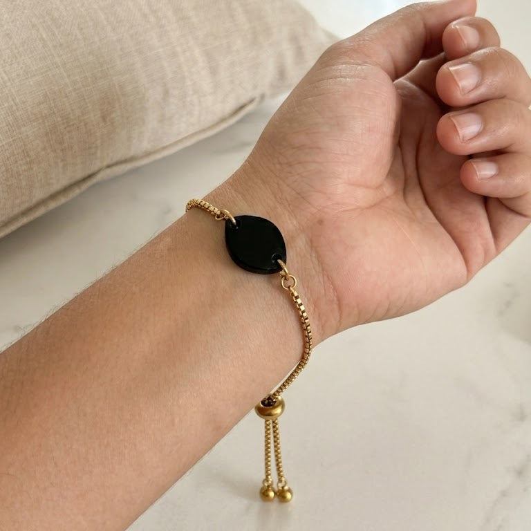 Gold bracelet with black charm on a wrist.